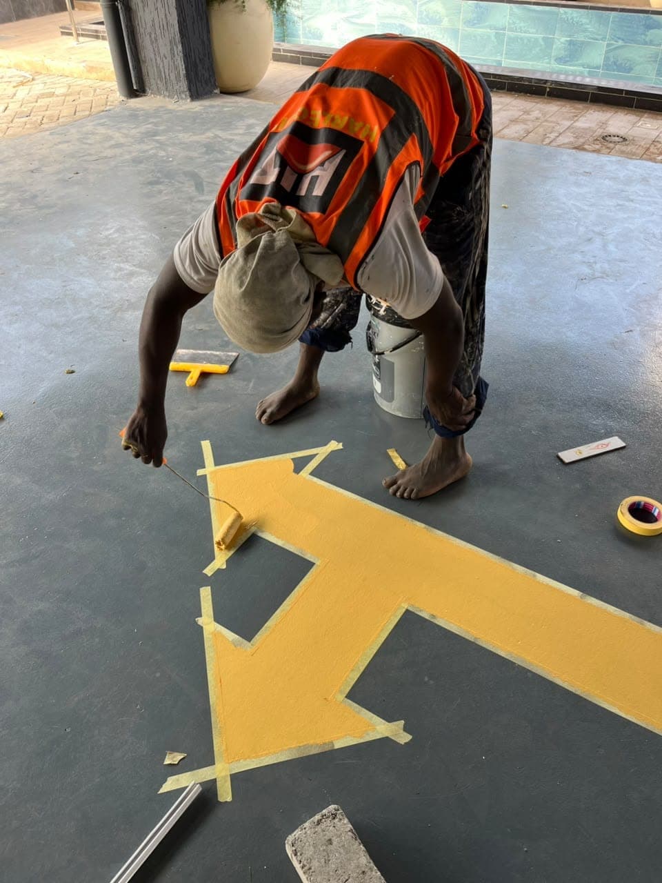 Painter applying a yellow directional arrow to a car park floor